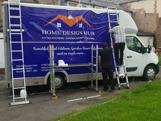 Two fitters on ladders applying printed graphics to the Home Design Hub box van
